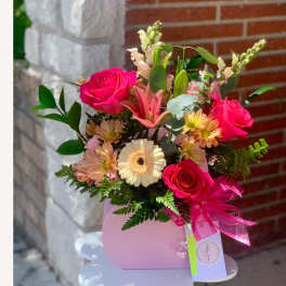 Pink floral arrangement in a purse-shaped container with a ribbon