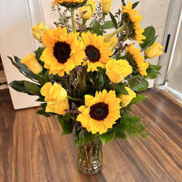 Tall vase arrangement of yellow sunflowers and yellow roses with a small card.