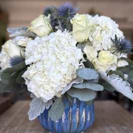 White hydrangeas and pale roses in a blue glass vase