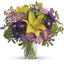 Yellow lilies and purple-pink daisies in a clear glass vase