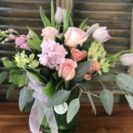 Pink roses and tulips arranged in a glass vase with ribbon