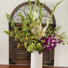 Tall floral arrangement in a white vase with white, green, yellow, and purple blooms