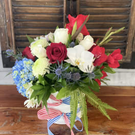 Red, white, and blue floral arrangement in a white vase with ribbon