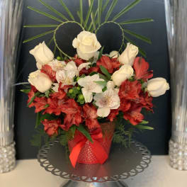 Red and white floral arrangement in a red vase with a ribbon