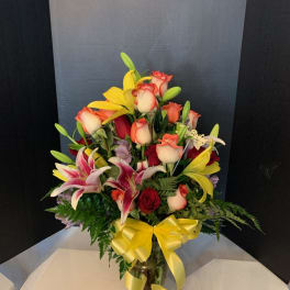 Mixed bouquet of roses and lilies in a glass vase with a yellow ribbon