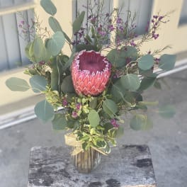 Protea bouquet in a glass vase with eucalyptus and purple filler flowers