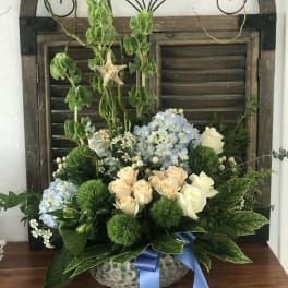 Blue hydrangeas and cream roses in a glass bowl with a blue ribbon