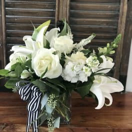 White lilies and roses in a glass vase with a striped ribbon