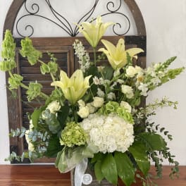 White and green floral arrangement with lilies and roses in a wooden container