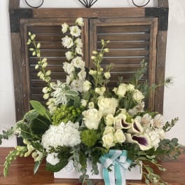 White floral arrangement in a white box with a teal ribbon