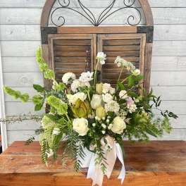 White and green floral arrangement in a white container with ribbon