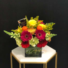 Bright mixed bouquet in a square glass vase with yellow, pink, and red blooms
