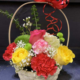 Basket arrangement of colorful roses and carnations with a red ribbon bow
