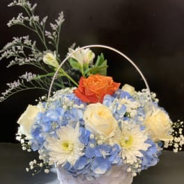 Basket of blue hydrangeas, white roses, and an orange rose