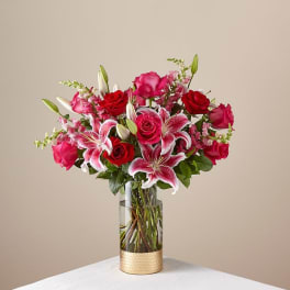 Pink and red roses with lilies in a clear glass vase