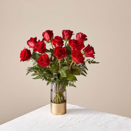 Red roses arranged in a clear glass vase with greenery