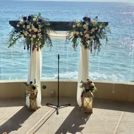 Wedding arch with white and burgundy floral arrangements overlooking the ocean