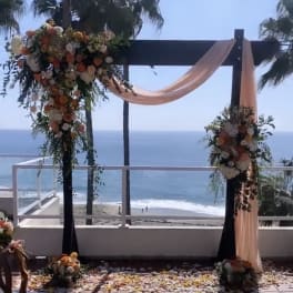 Floral wedding arch with peach draping overlooking the ocean