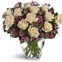 Arrangement of cream roses with small purple flowers in a clear glass vase