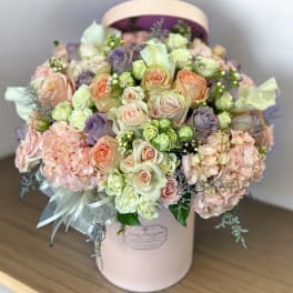 Pastel roses and hydrangeas arranged in a pink hat box with ribbon