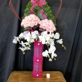 Pink roses and white orchids arranged in a tall decorative vase with a heart frame