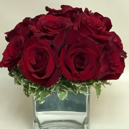 Red roses arranged in a clear glass vase with variegated greenery
