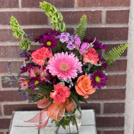 Mixed pink, purple, and orange flowers in a glass vase with a ribbon