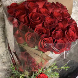 Bouquet of red roses wrapped in clear plastic with greenery