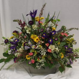 Mixed floral arrangement in a rectangular container with purple, yellow, pink, and white blooms