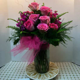 Pink roses arranged in a tall glass vase with a pink ribbon