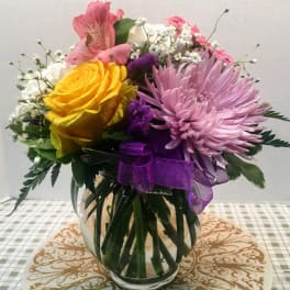 Bouquet of yellow and pink flowers in a glass vase with a purple ribbon