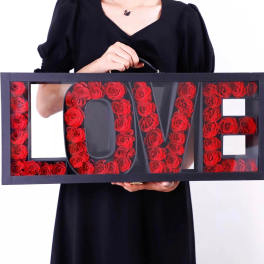 Framed LOVE sign filled with red roses, held by a person in black