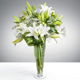 Tall clear vase of white lilies with green accents and looped striped leaves