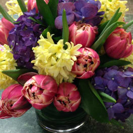 Bouquet of pink tulips, purple hydrangeas, and yellow flowers in a glass vase
