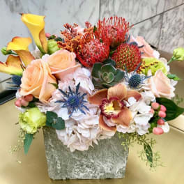 Mixed floral arrangement with roses, calla lilies, orchids, and succulents in a stone vase.