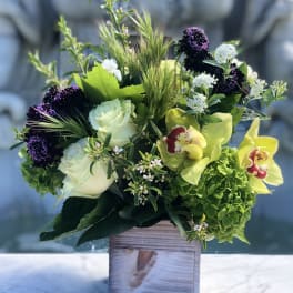 Arrangement of green hydrangea, white roses, and yellow orchids in a rustic wooden cube vase