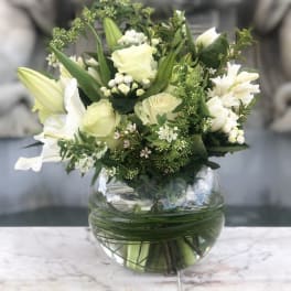 White and pale green floral arrangement in a round glass vase