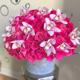 Round hatbox arrangement of bright pink roses accented with pale pink orchids