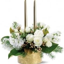 White floral arrangement in a gold container with two tall candles