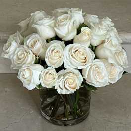 Compact arrangement of ivory white roses in a clear glass cylinder vase