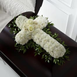 White floral cross arrangement on a dark casket