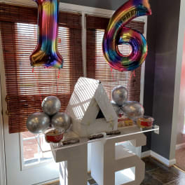 Rainbow balloons shaped like 1 and 6 above a decorated table