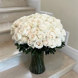 Large arrangement of white and cream roses in a clear glass vase on marble steps
