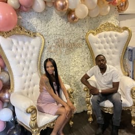 Balloon backdrop with two ornate white-and-gold chairs and seated couple