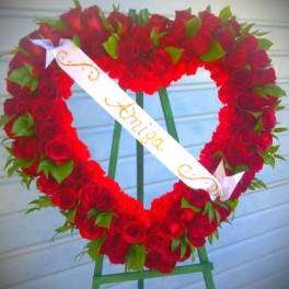 Heart-shaped wreath of red roses with a white ribbon on an easel