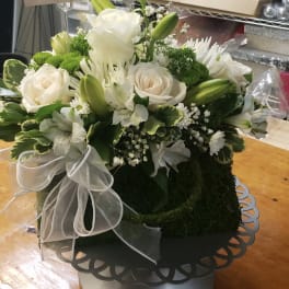 White roses and lilies arranged in a round box with a white ribbon