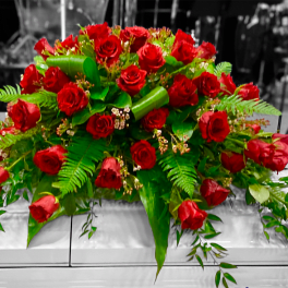 Large arrangement of red roses with green foliage on a white casket