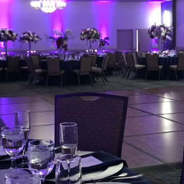 Banquet hall with tall floral centerpieces on round tables under purple lighting