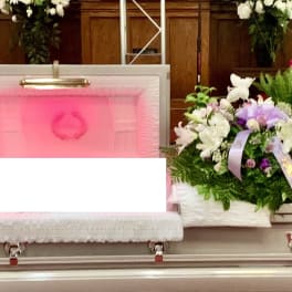 White casket surrounded by purple and white funeral flower sprays