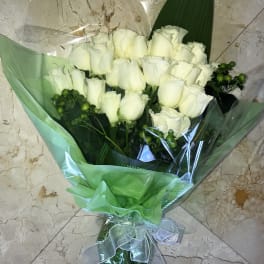 Bouquet of white roses with green berry accents wrapped in green and clear cellophane.